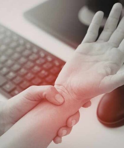 Persona sujetando la muñeca con molestia junto a laptop, señal de dolor por uso repetitivo.