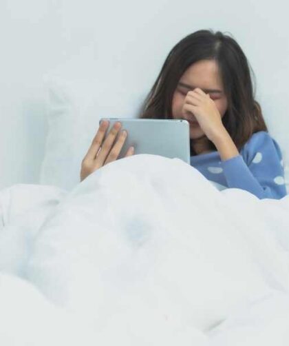 Chica recostada en su cama frotándose los ojos por cansancio provocado por su IPAD
